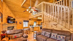 Ein Blockhaus mit Holzausstattung, Kamin, einer Couch, einem Fernseher und einer Treppe.