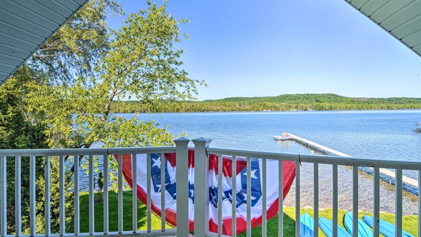 A view from a covered porch overlooking a lake with kayaks and an American flag. - Lakefront Bellaire Getaway w/ Kayaks, Dock & Grill (Bellaire)