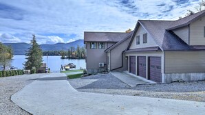 A two-story house with a garage, a driveway, and a lake view. - Lake George Getaway w/ Mountain + Water Views (Bolton Landing)
