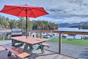 A wooden deck with a picnic table and benches, overlooking a lake with boats and a dock. - Lake George Getaway w/ Mountain + Water Views (Bolton Landing)