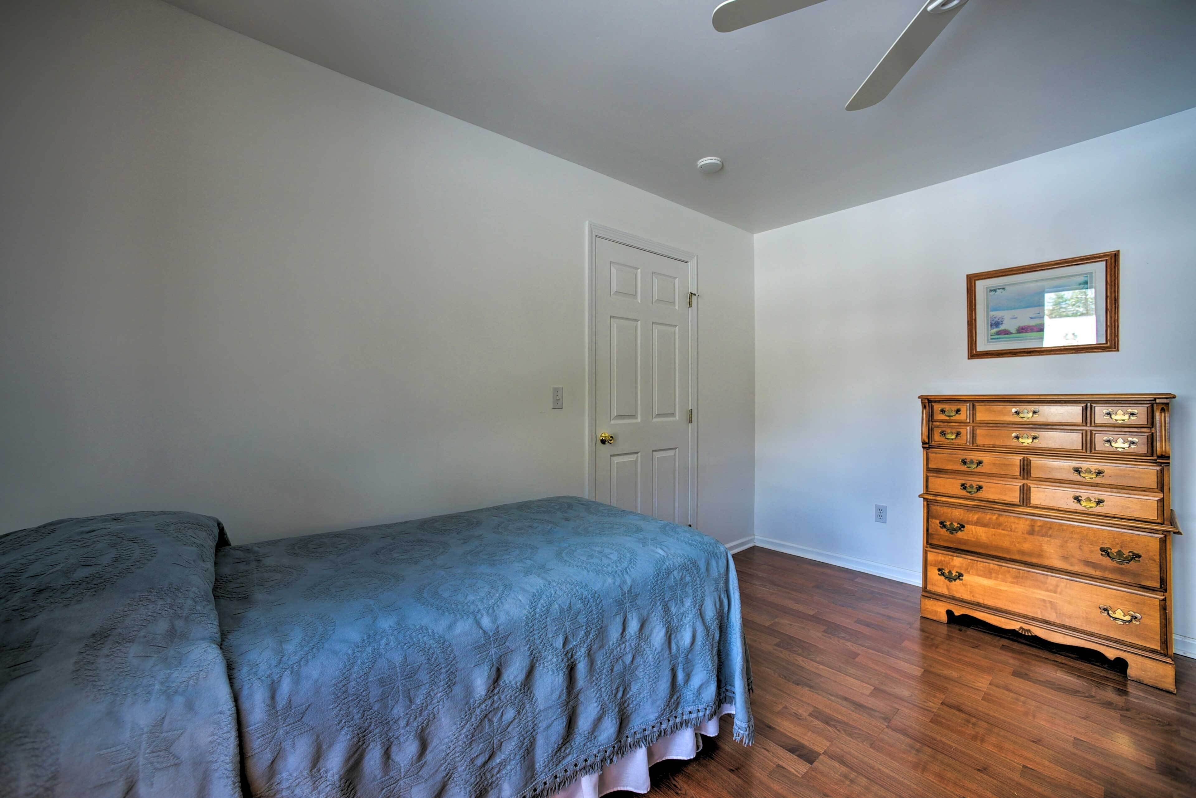 A bedroom with a bed, a dresser, a door, and a ceiling fan.
