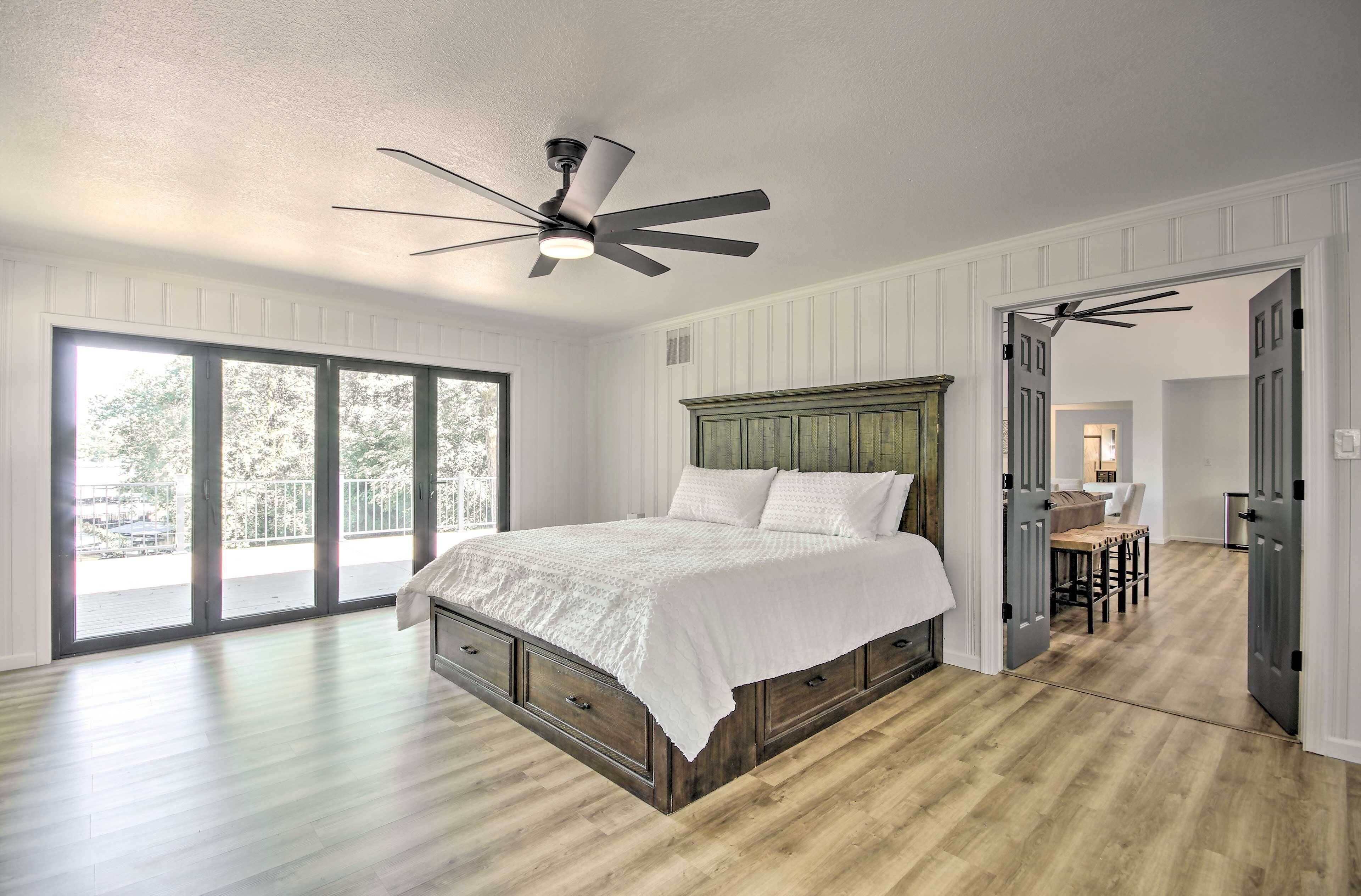 A bedroom with a large bed, a ceiling fan, and a view through a sliding glass door to the outside.