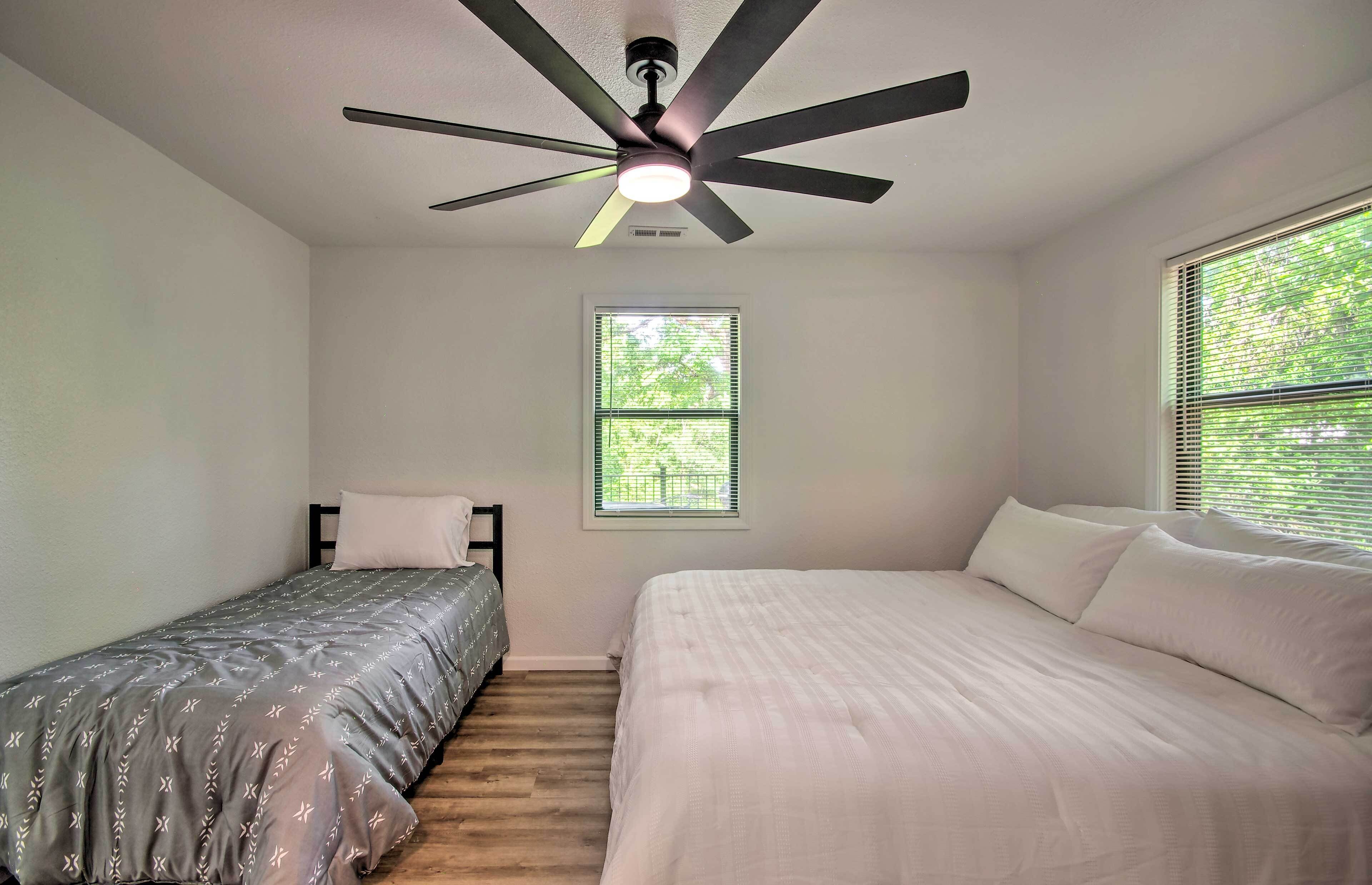 A bedroom with a ceiling fan, a window with blinds, a bed, and a smaller bed.