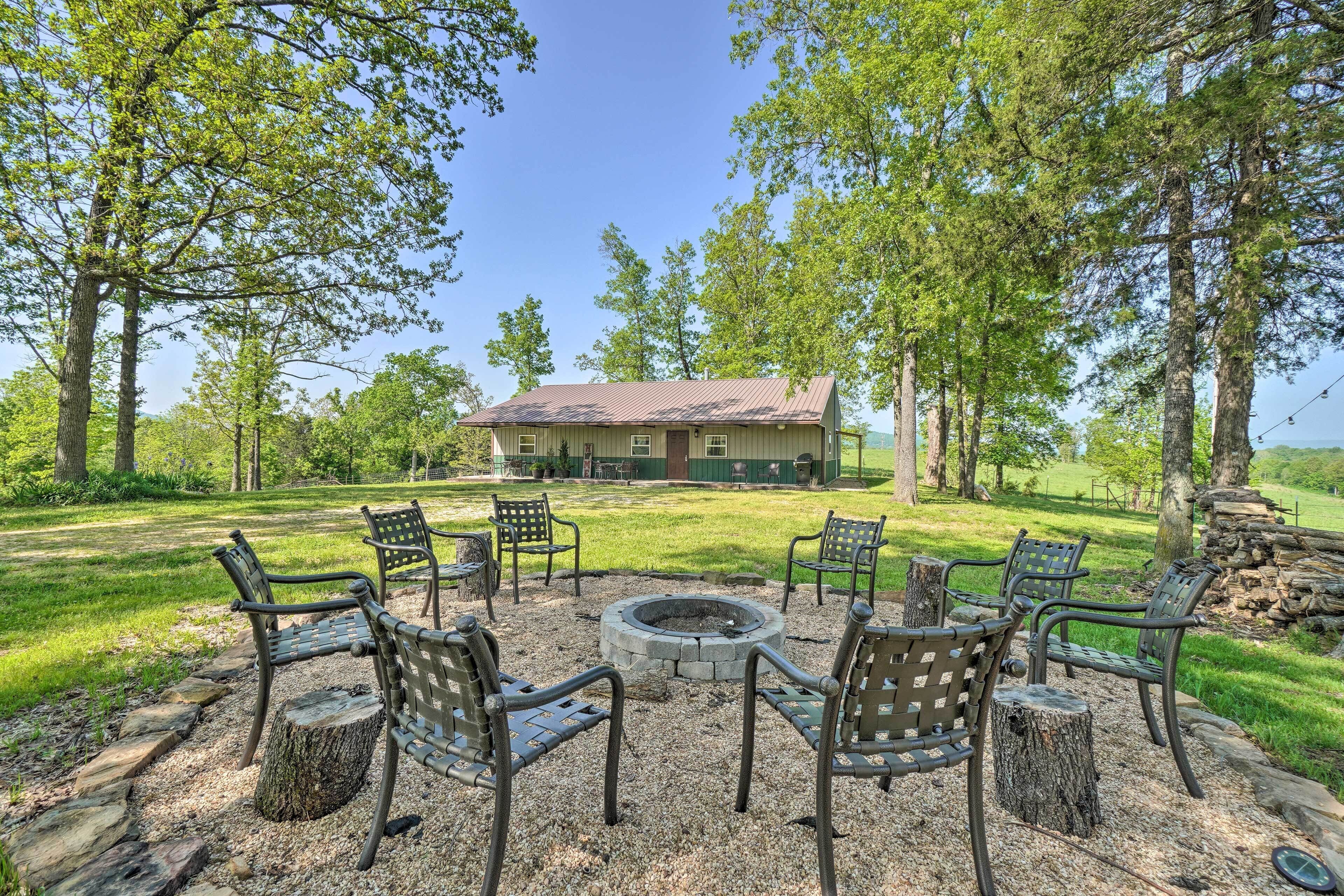 A fire pit surrounded by six metal chairs, a stone fire pit, and a house in the background.