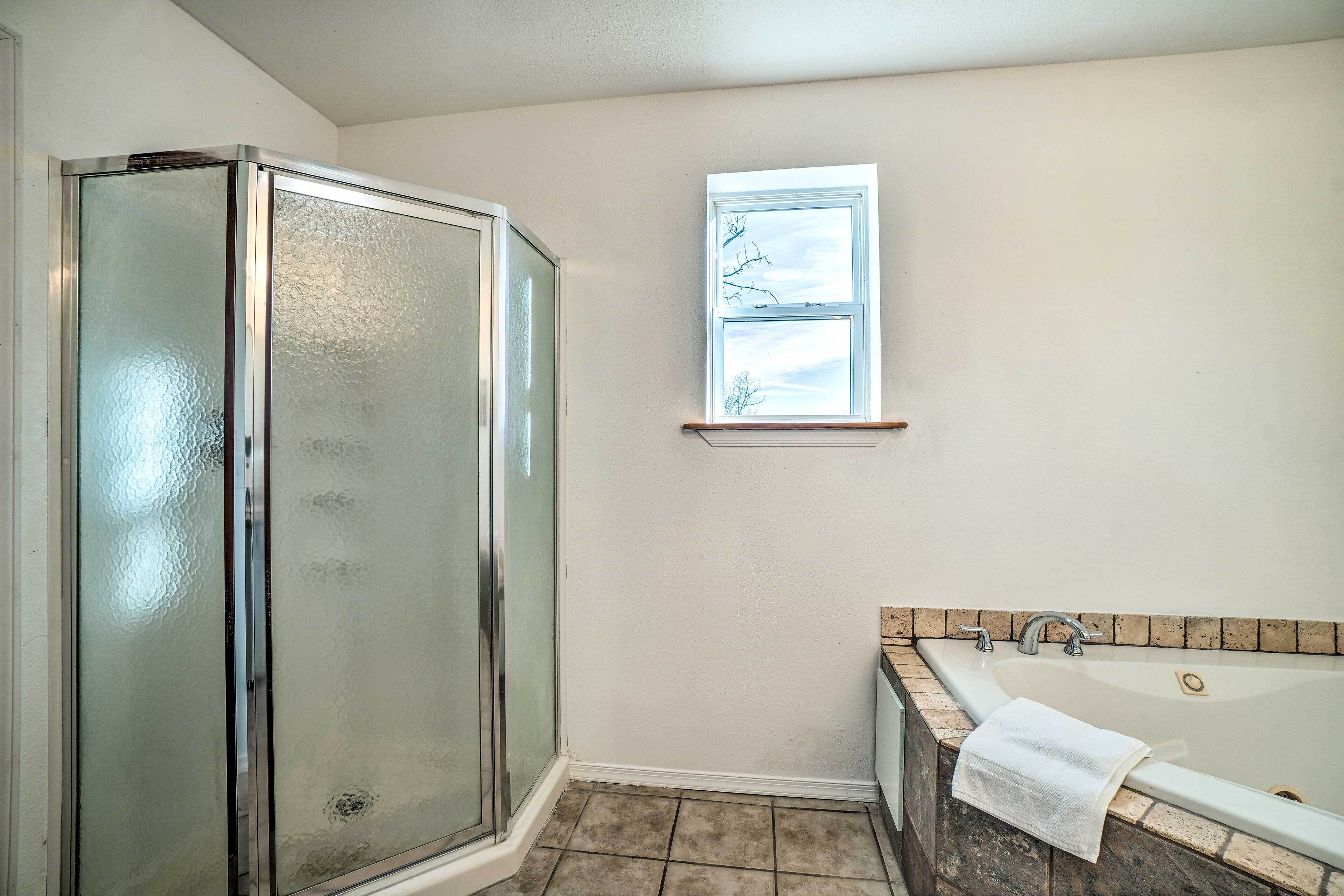 Un baño con cabina de ducha de vidrio, bañera con toalla y ventana con vistas.