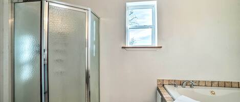 Un baño con cabina de ducha de vidrio, bañera con toalla y ventana con vistas.