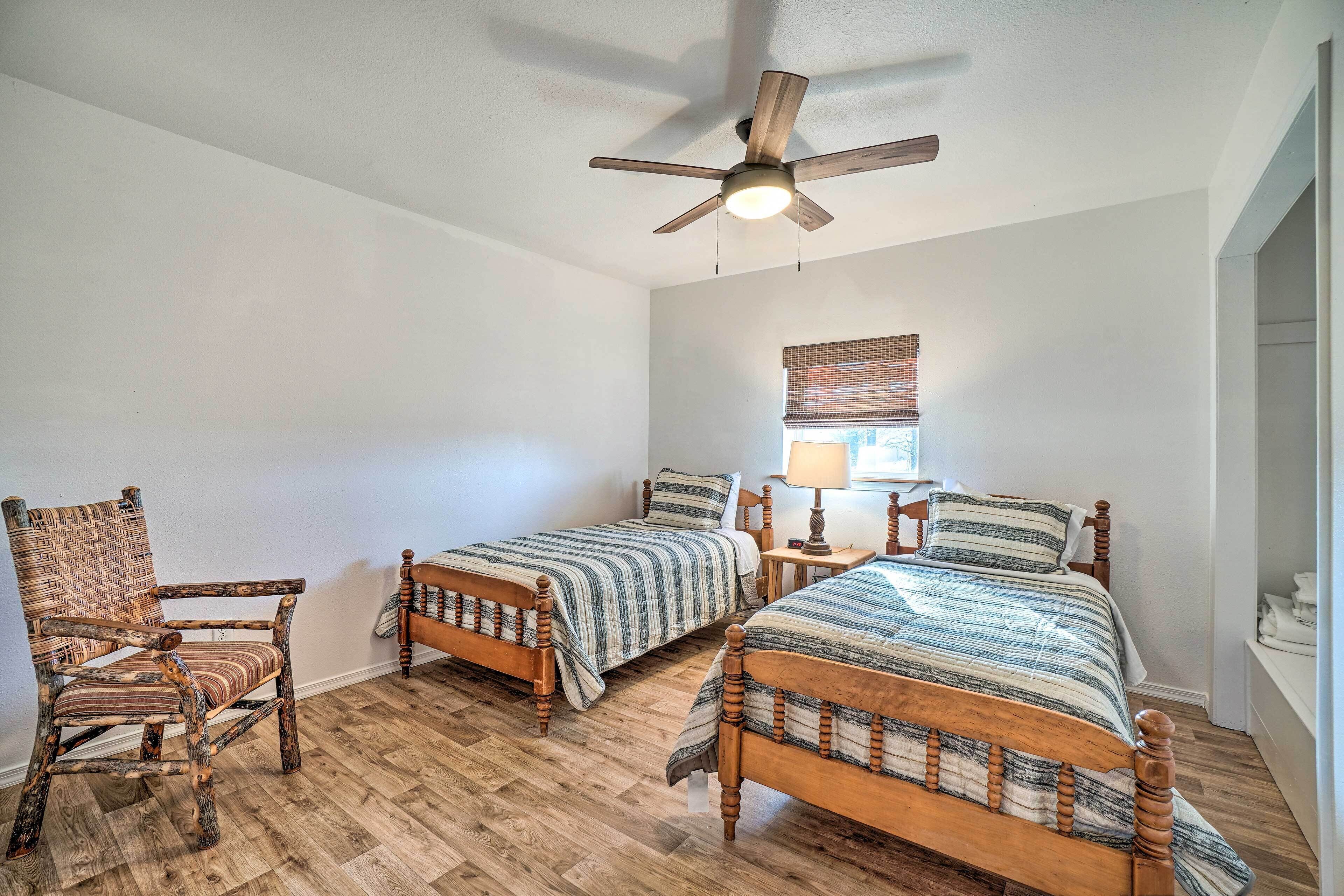 A bedroom with two wooden beds, a wooden chair, a ceiling fan, and a window with blinds.