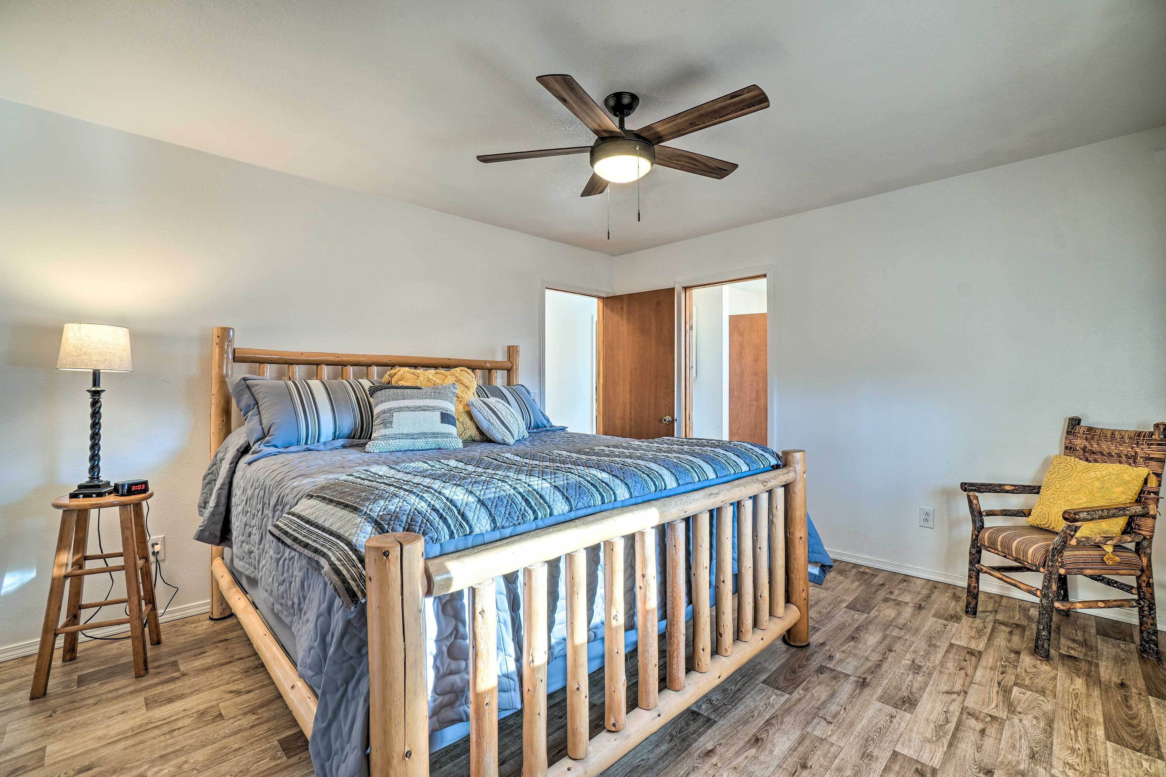 A bedroom with a wooden bed, a ceiling fan, a nightstand with a lamp, and a chair with a cushion.