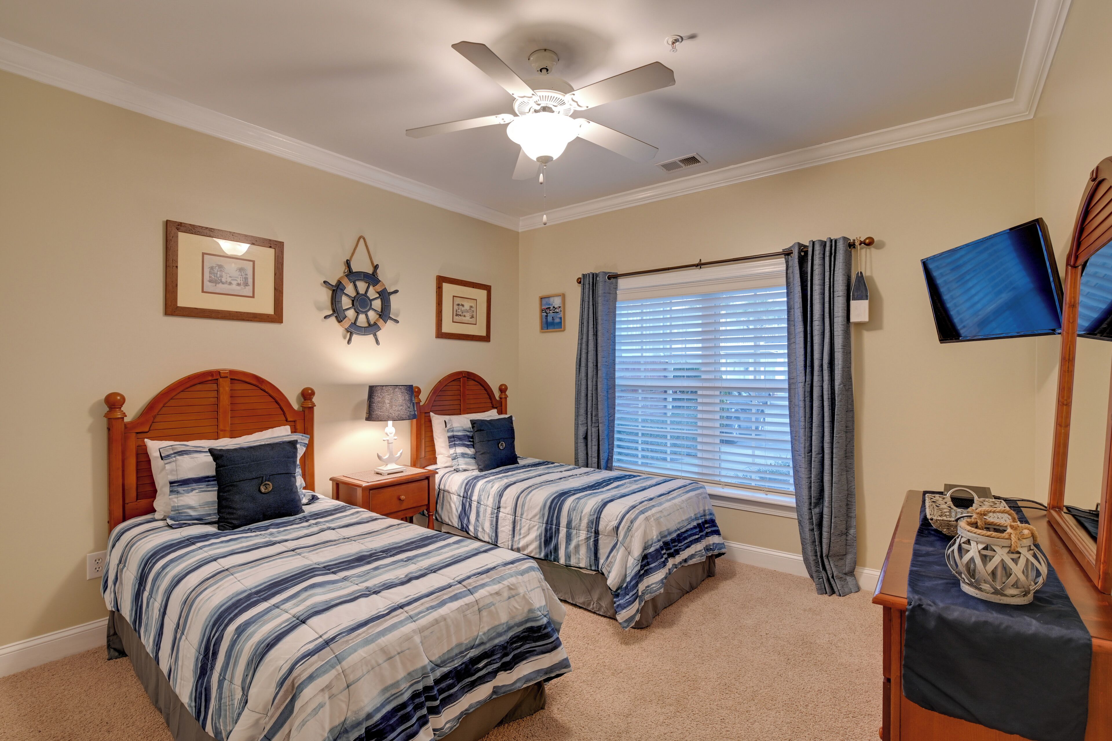 A bedroom with two beds, a ceiling fan, a window with blinds, and a TV mounted on the wall.