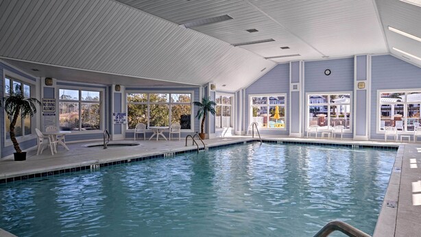 En inomhuspool med stora fönster, vita väggar och ett kaklat golv.