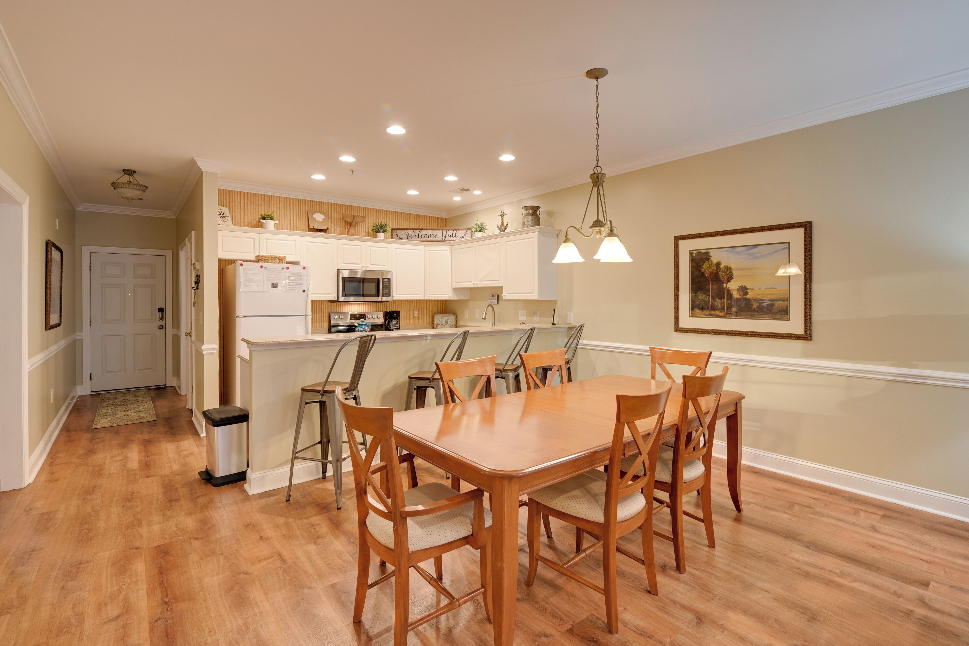 A modern kitchen with white cabinets, a central island, and a dining area with wooden chairs.