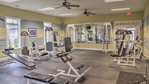 Ett gym med olika typer av träningsutrustning, takfläktar och stora fönster.