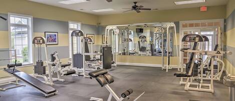 A gym with various exercise equipment, ceiling fans, and large windows.