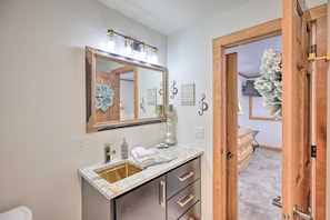 A bathroom with a marble sink, a large mirror with lights, and a wooden door leading to another room. - Regal River Retreat in the Heart of Yankton! (Yankton)