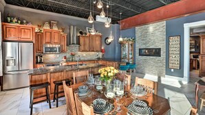 Una cocina amplia con armarios de madera, una isla central y un comedor con una gran mesa de madera preparada para seis comensales.