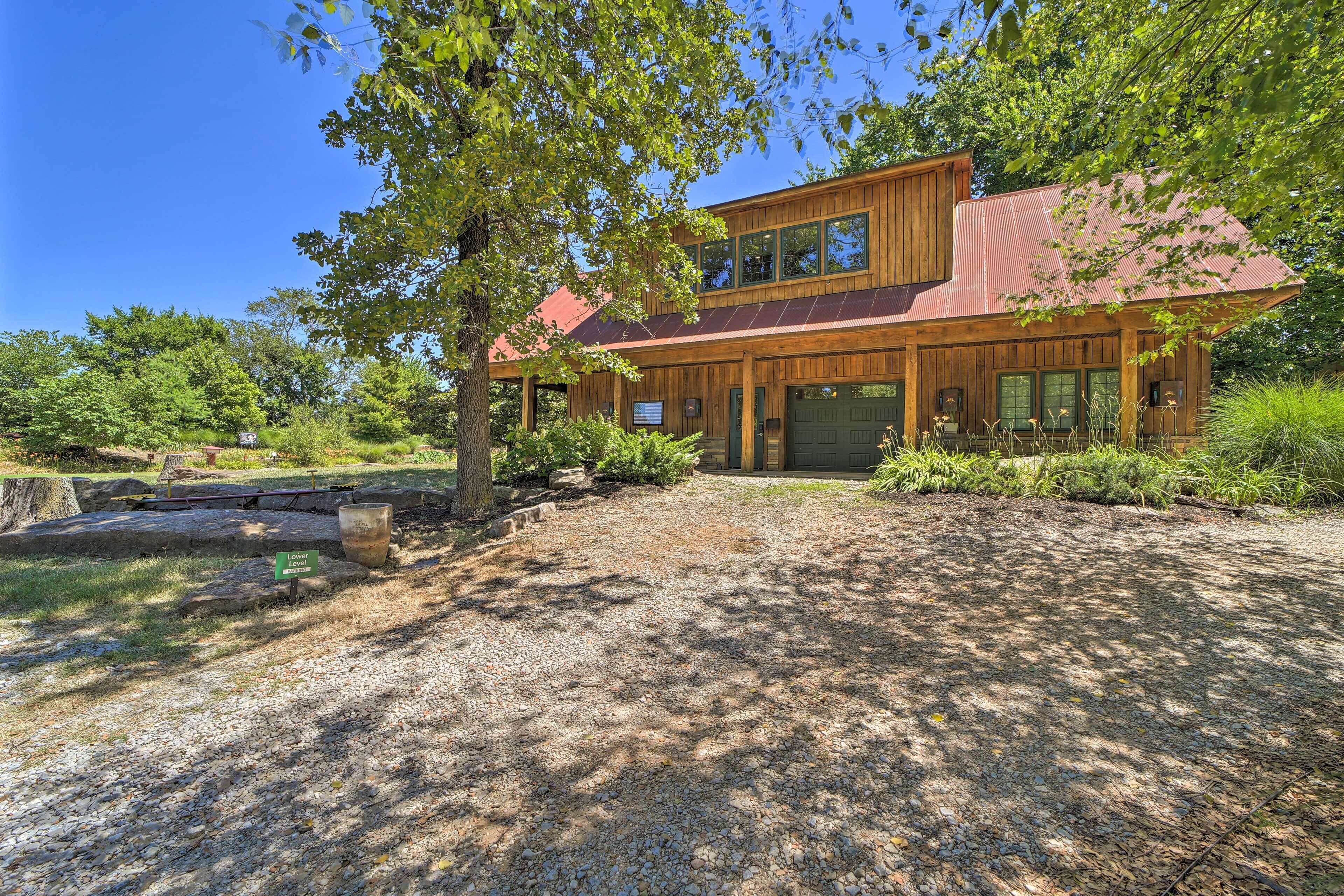 A two-story wooden house with a red roof, surrounded by trees and a gravel driveway.
