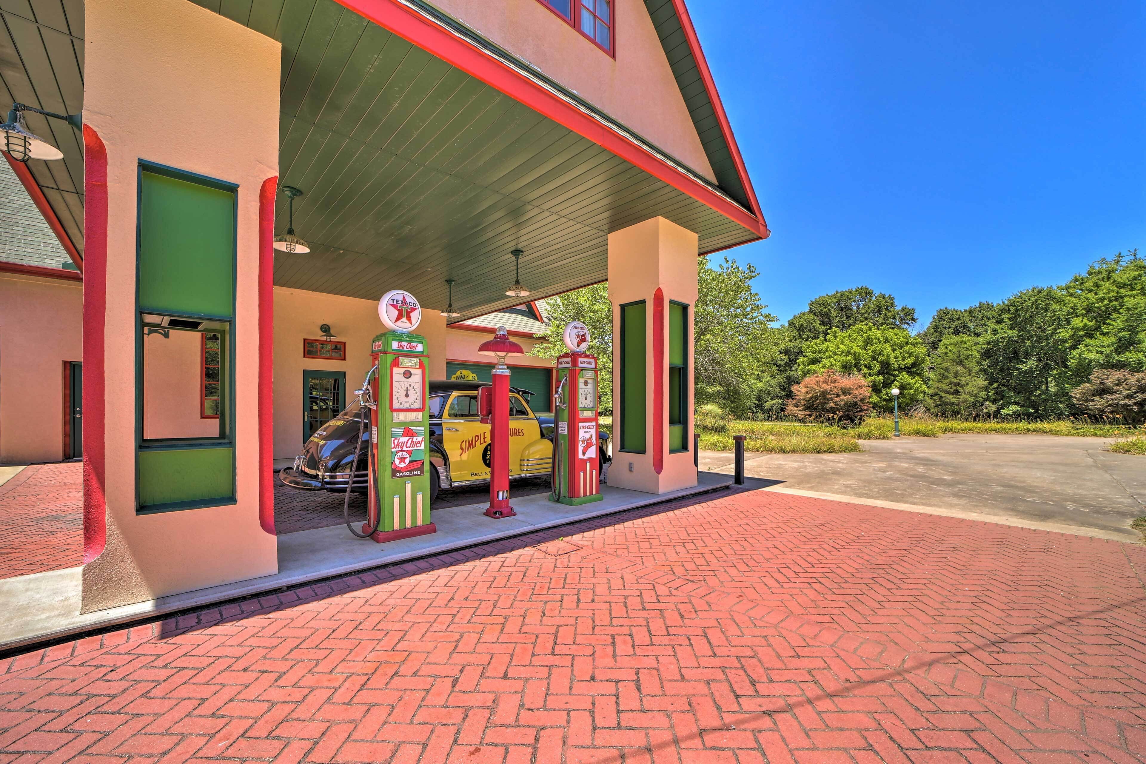 Una gasolinera de estilo antiguo con fachada de ladrillo rojo, un coche amarillo estacionado en su interior y un cielo azul claro al fondo.
