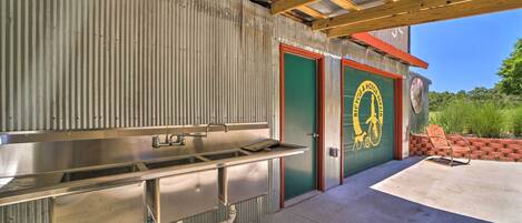 A covered outdoor kitchen area with stainless steel appliances, a brick wall, and a door with a bicycle logo.