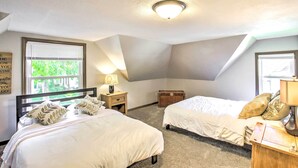 A bedroom with two beds, a window with blinds, a bedside table with a lamp, and a small wooden chest. - Appleton Abode Near Lake Winnebago & Downtown (Appleton)