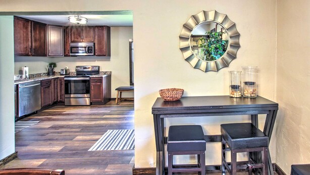 A modern kitchen with wooden cabinets, stainless steel appliances, and a dining area with a black table and two chairs. - Appleton Abode Near Lake Winnebago & Downtown (Appleton)