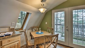 Comedor con mesa y sillas de madera, lámpara en el techo y ventanas amplias con vista a árboles.