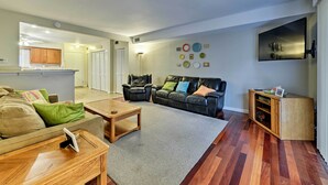 A living room with a sofa, coffee table, and TV stand. There is a door leading to another room. - Family-friendly Wildwood Townhome ~ 3 Mi to Beach (Wildwood)