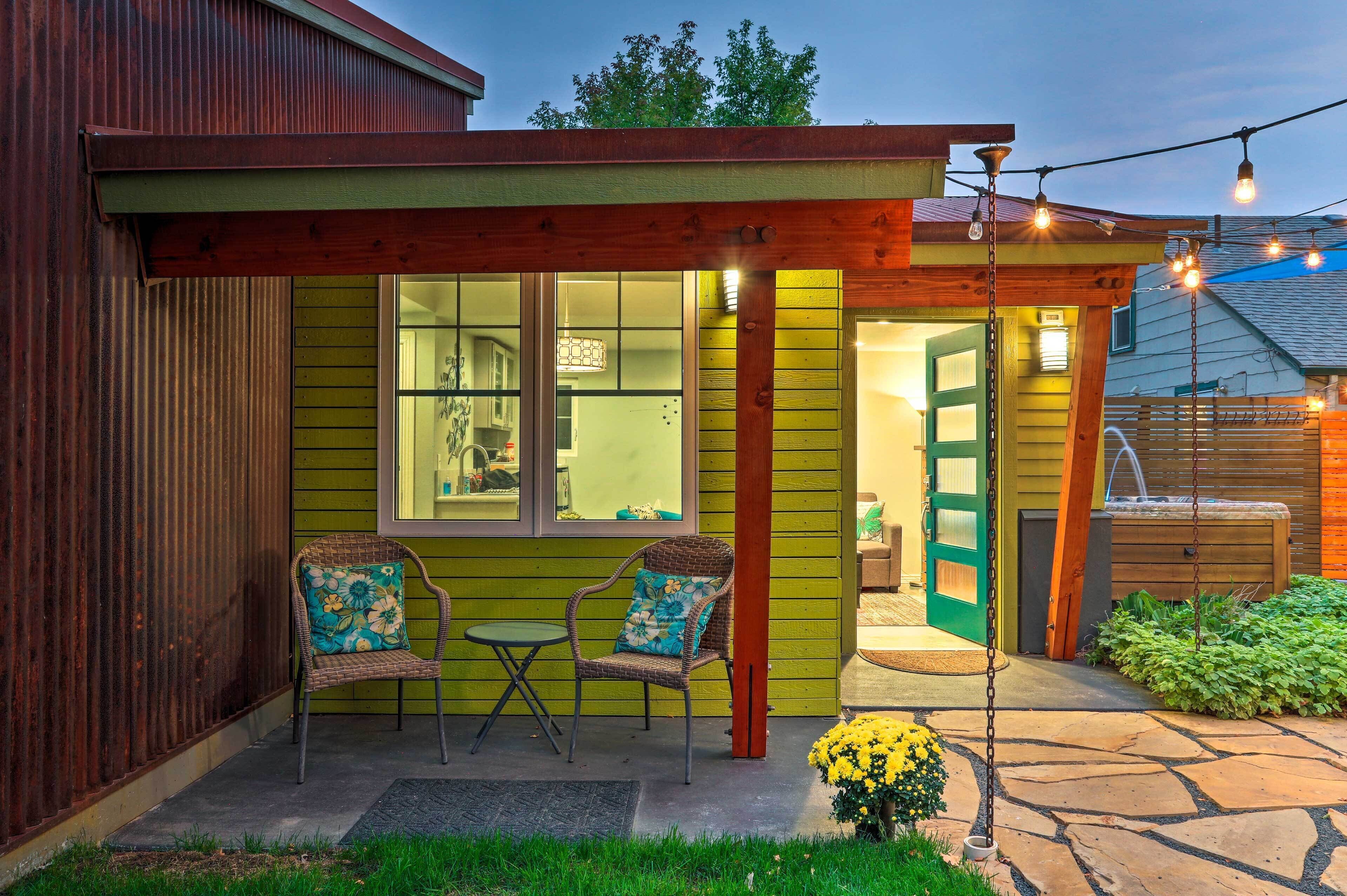 A cozy outdoor seating area with two wicker chairs and a small table, a wooden pergola, and a string of lights.