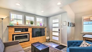 A living room with a fireplace, a television, and a seating area with a blue armchair and a grey sofa. - Fort Collins Vacation Rental w/ Private Hot Tub! (Fort Collins)