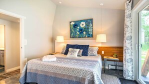 A bedroom with a bed, two bedside lamps, a painting above the bed, and a view of the outdoors through a window. - Fort Collins Vacation Rental w/ Private Hot Tub! (Fort Collins)