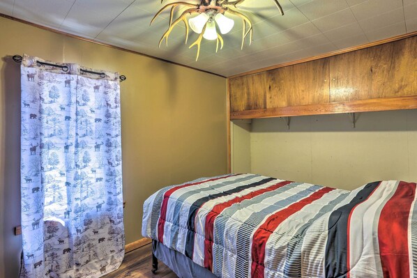 Quarto com cama, cabeceira de madeira, cortina estampada e luminária no teto.