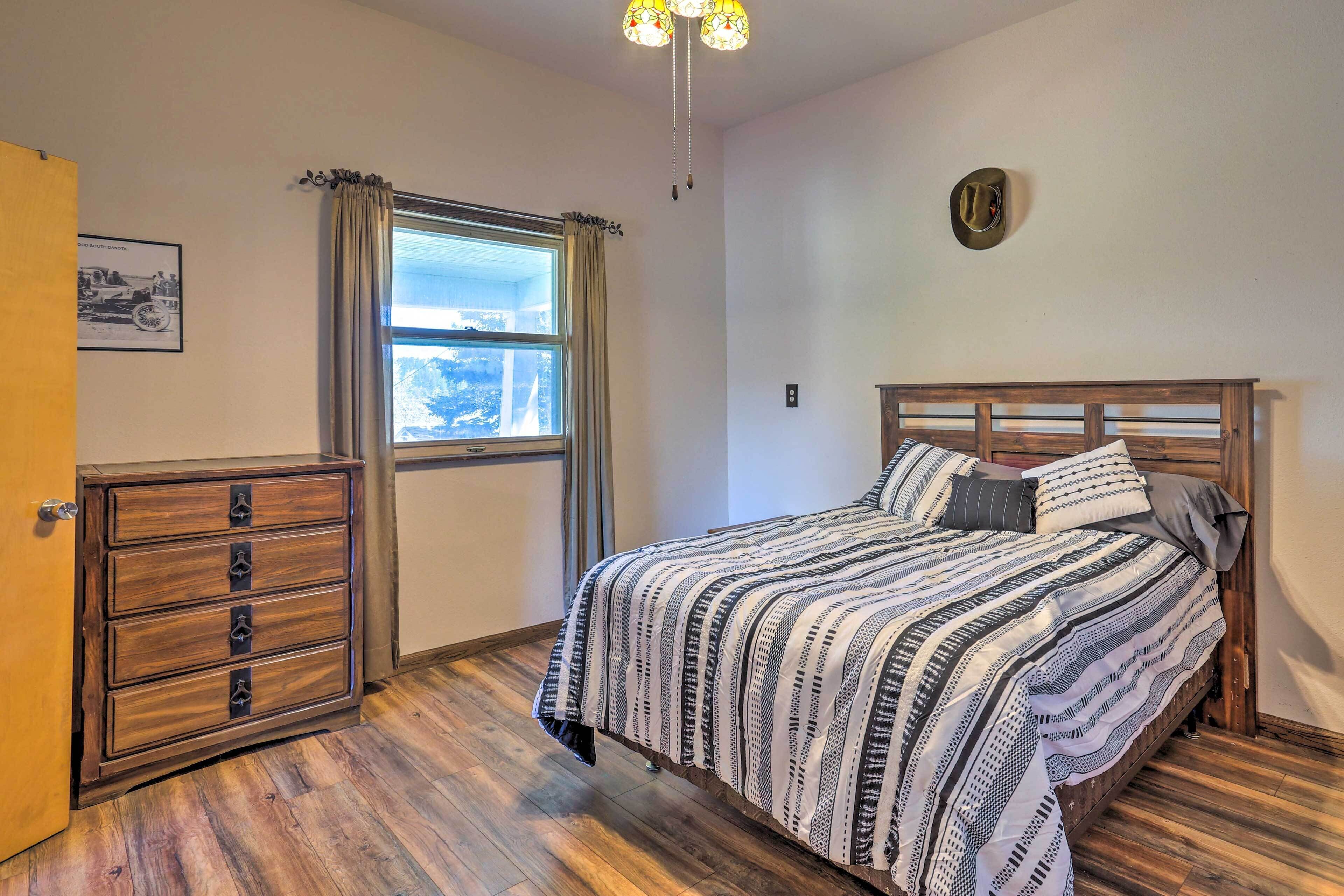 A bedroom with a wooden bed, a dresser, a window with curtains, and a ceiling light fixture.