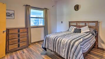 A bedroom with a wooden bed, a dresser, a window with curtains, and a ceiling light fixture.