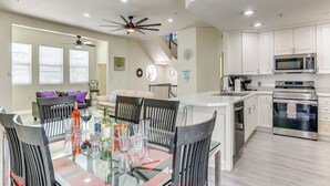 A modern kitchen with white cabinets, stainless steel appliances, and a glass dining table. - Clearwater Beach Hideaway: Walkable Location! (Clearwater Beach)