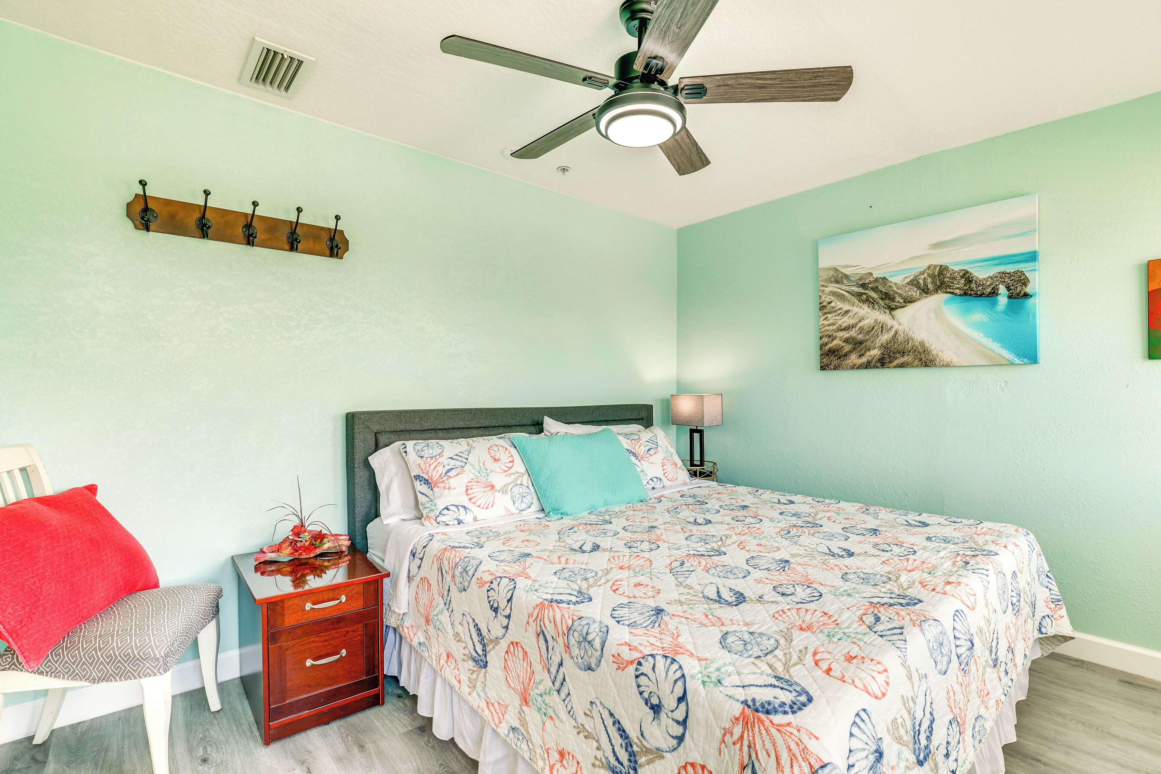 A bedroom with a bed, a nightstand, a chair, a ceiling fan, and a wall-mounted coat rack.