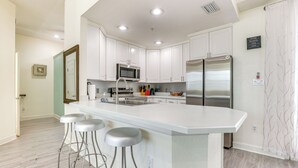 A modern kitchen with white cabinets, stainless steel appliances, and a bar area with stools. - Clearwater Beach Hideaway: Walkable Location! (Clearwater Beach)