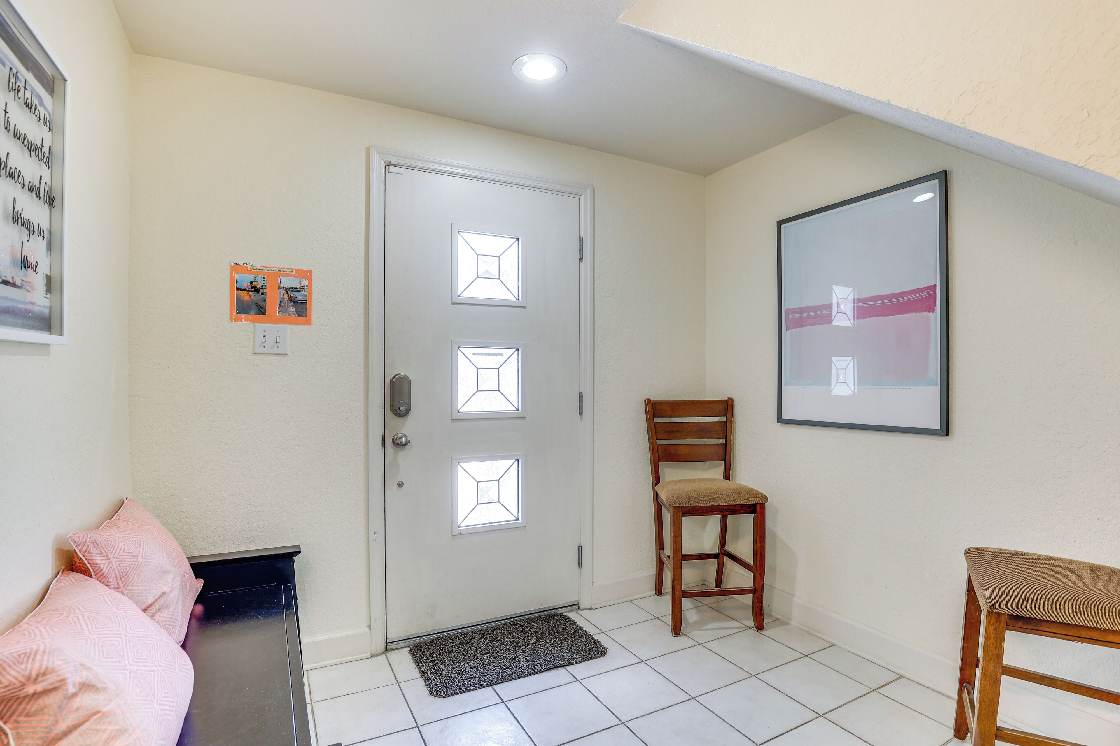 Ein Zimmer mit weißer Tür, einem gerahmten Bild an der Wand, einem Holzstuhl und einer Bank.