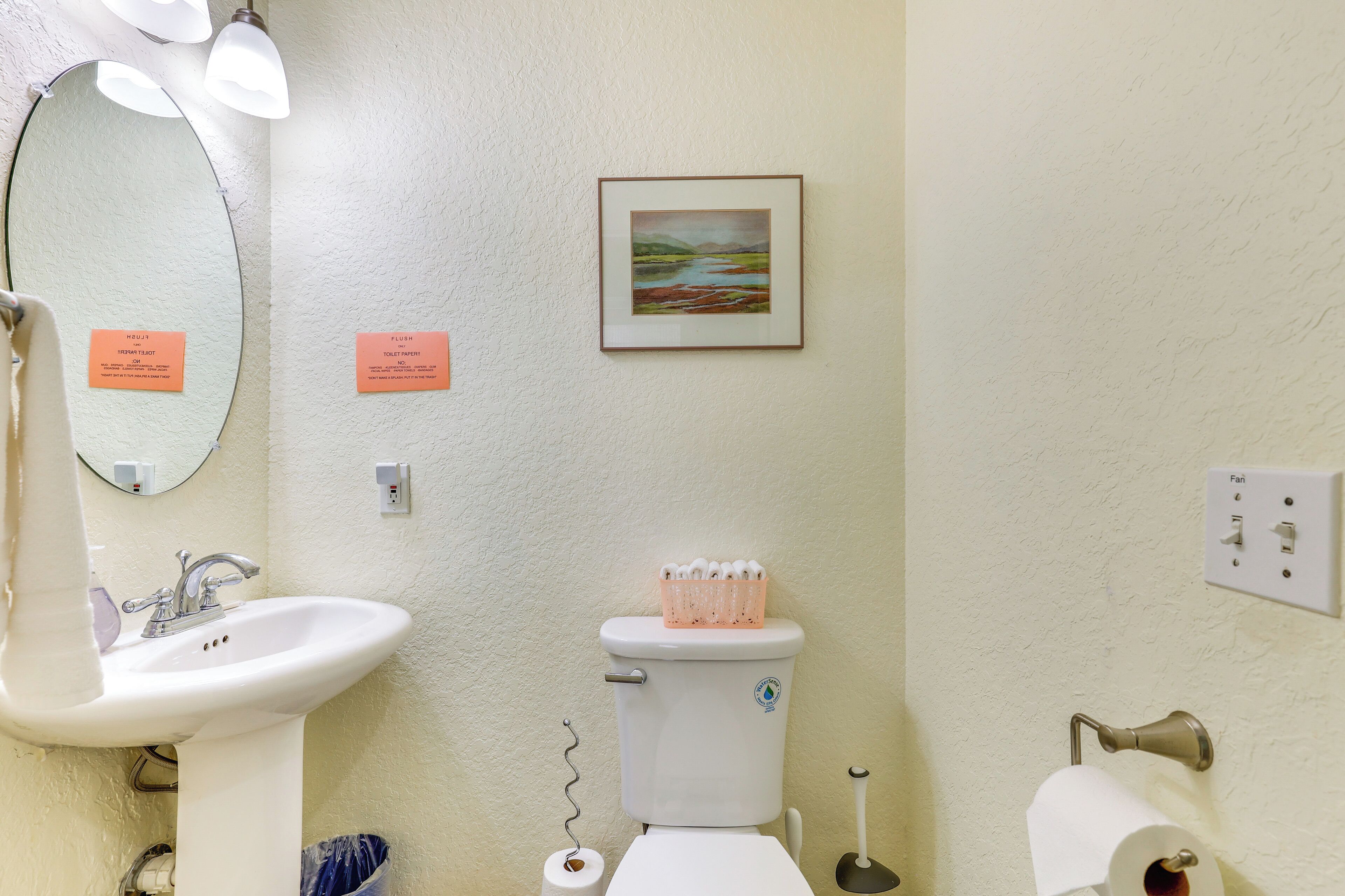 Un baño con lavamanos, inodoro y un cuadro con paisaje en la pared.
