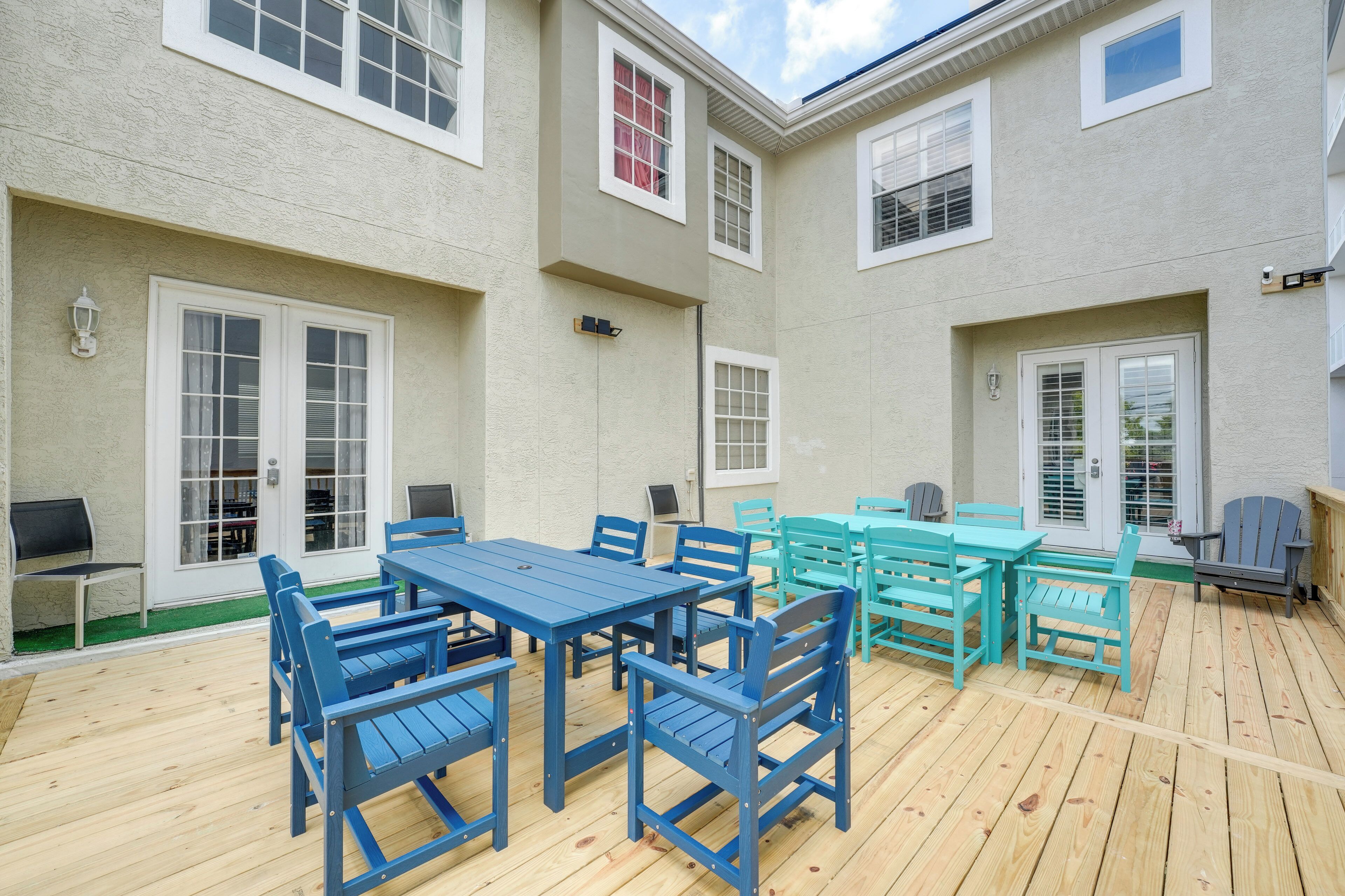 A covered patio with a wooden deck, outdoor seating, and a building with multiple windows and doors.