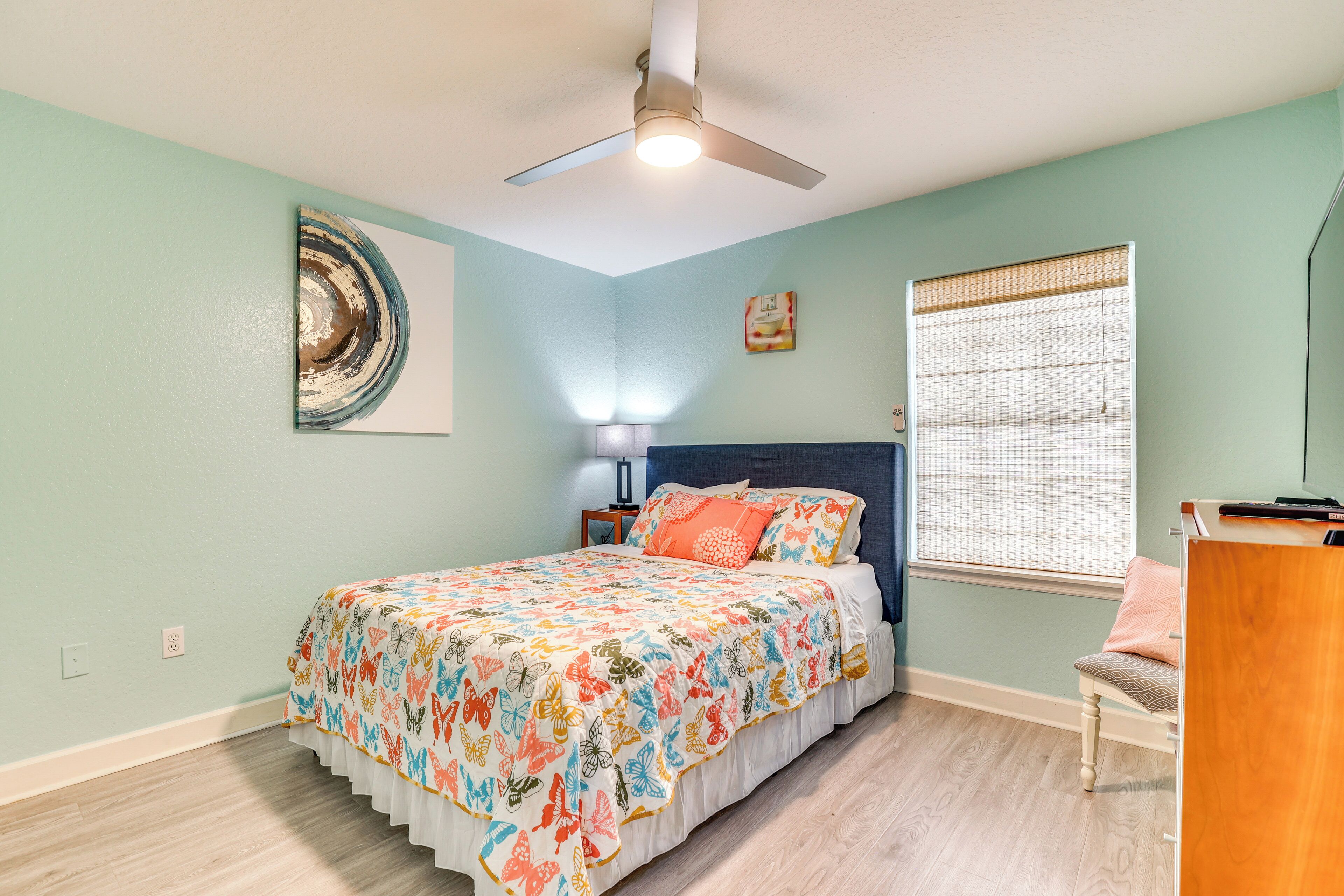 A bedroom with a bed, a nightstand, a chair, a ceiling fan, and a window with blinds.