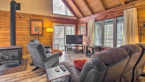 A cozy cabin interior with a fireplace, comfortable seating, a television, and large windows.