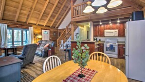 A spacious living area with a wooden ceiling, a dining table with chairs, a fireplace, and a kitchen with modern appliances.