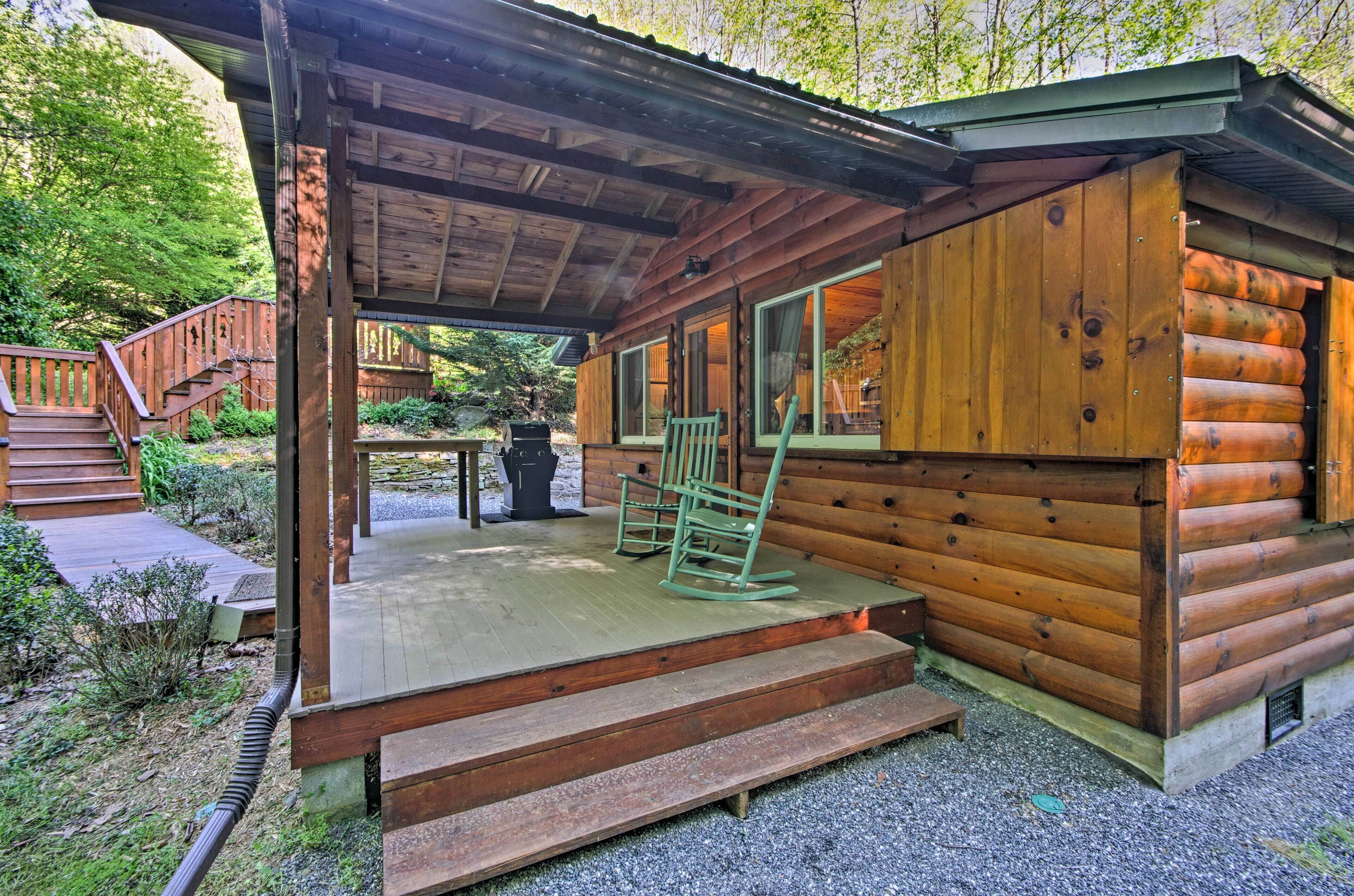 A wooden cabin with a porch, a staircase leading to the entrance, and a small outdoor seating area.
