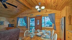 A wooden cabin with a dining table set for four, a sofa, a television, and a refrigerator. - Cabin by Bold Creek: Book Now for Polar Express! (Bryson City)