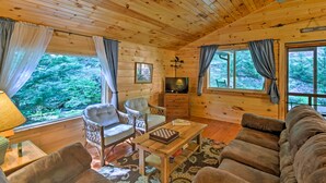 A cozy cabin interior with wooden walls, a sofa, a chair, a table, and a television. - Cabin by Bold Creek: Book Now for Polar Express! (Bryson City)