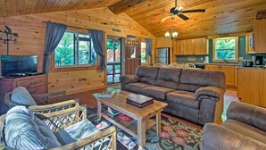 A cozy cabin interior with a wooden ceiling, a sofa, a coffee table, a television, and a kitchen area. - Cabin by Bold Creek: Book Now for Polar Express! (Bryson City)