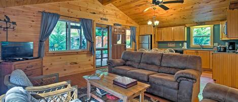 Un acogedor interior de cabaña con techo de madera, un sofá, una mesa de centro, un televisor y una zona de cocina.