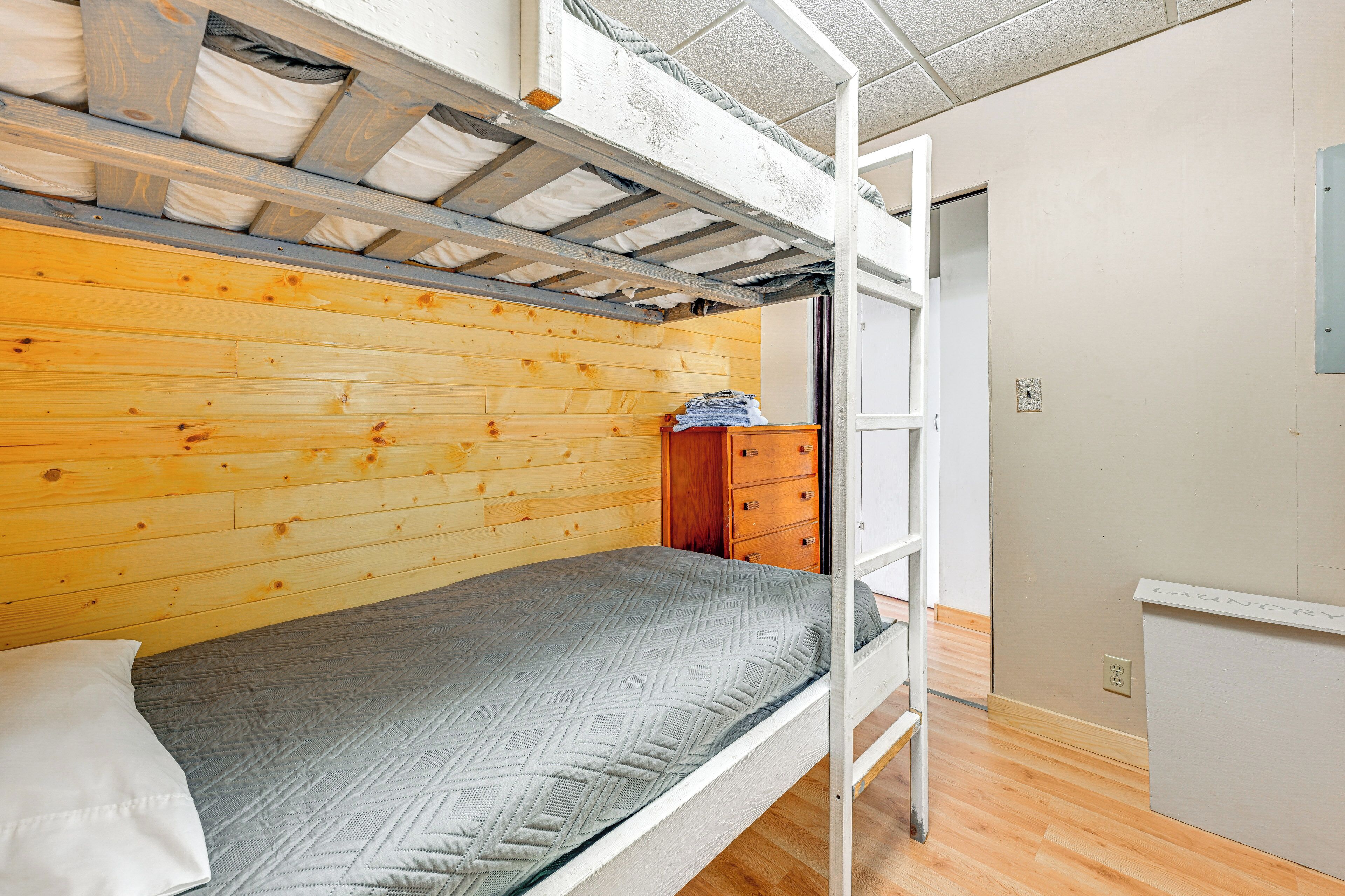 A bunk bed room with a wooden wall, a small wooden dresser, and a whiteboard labeled "Laundry".