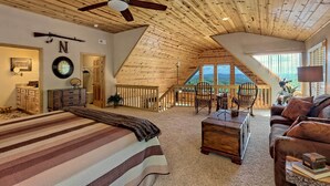 Une chambre spacieuse aménagée en mezzanine, dotée d’un grand lit, d’un plafond en bois et offrant une vue sur l’extérieur.