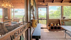 L’intérieur d’un chalet en bois, avec une pancarte « BIENVENUE », un banc en bois, une table à manger et une vue sur l’extérieur.