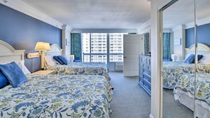 A hotel room with two beds, a dresser, a mirror, and a view of the city through large windows.
